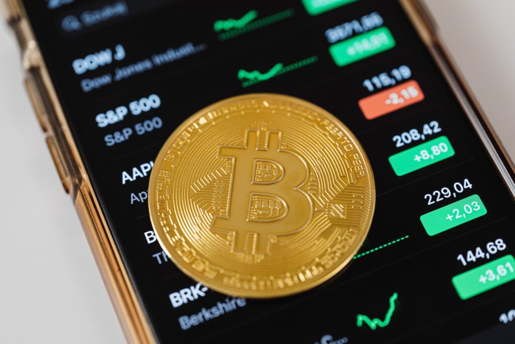  Bitcoin placed on a phone with stocks running below.