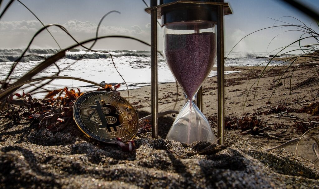 a bitcoin placed right by the side of a hourglass showing the time required for yield farming